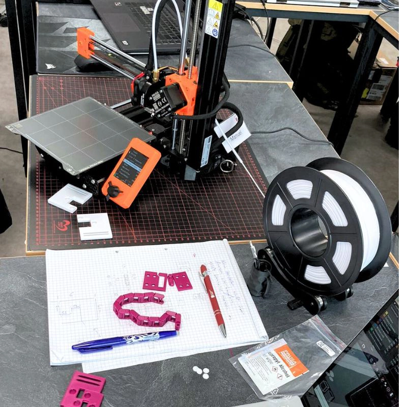 3D-Drucker mit Filamentspule, Zeichnungen und gefertigten Kunststoffteilen in einer technischen Lernumgebung des Technikums.