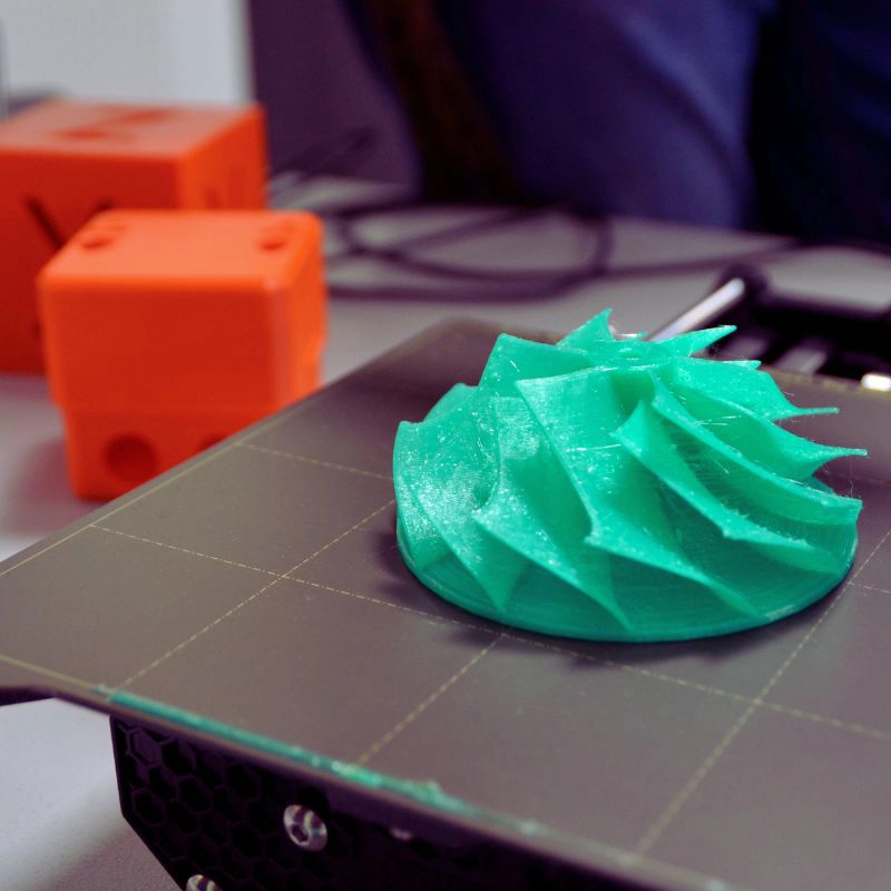 Detailaufnahme eines grün gedruckten Prototyps auf einer 3D-Druckerplatte im Technikum der German Academies Munich.