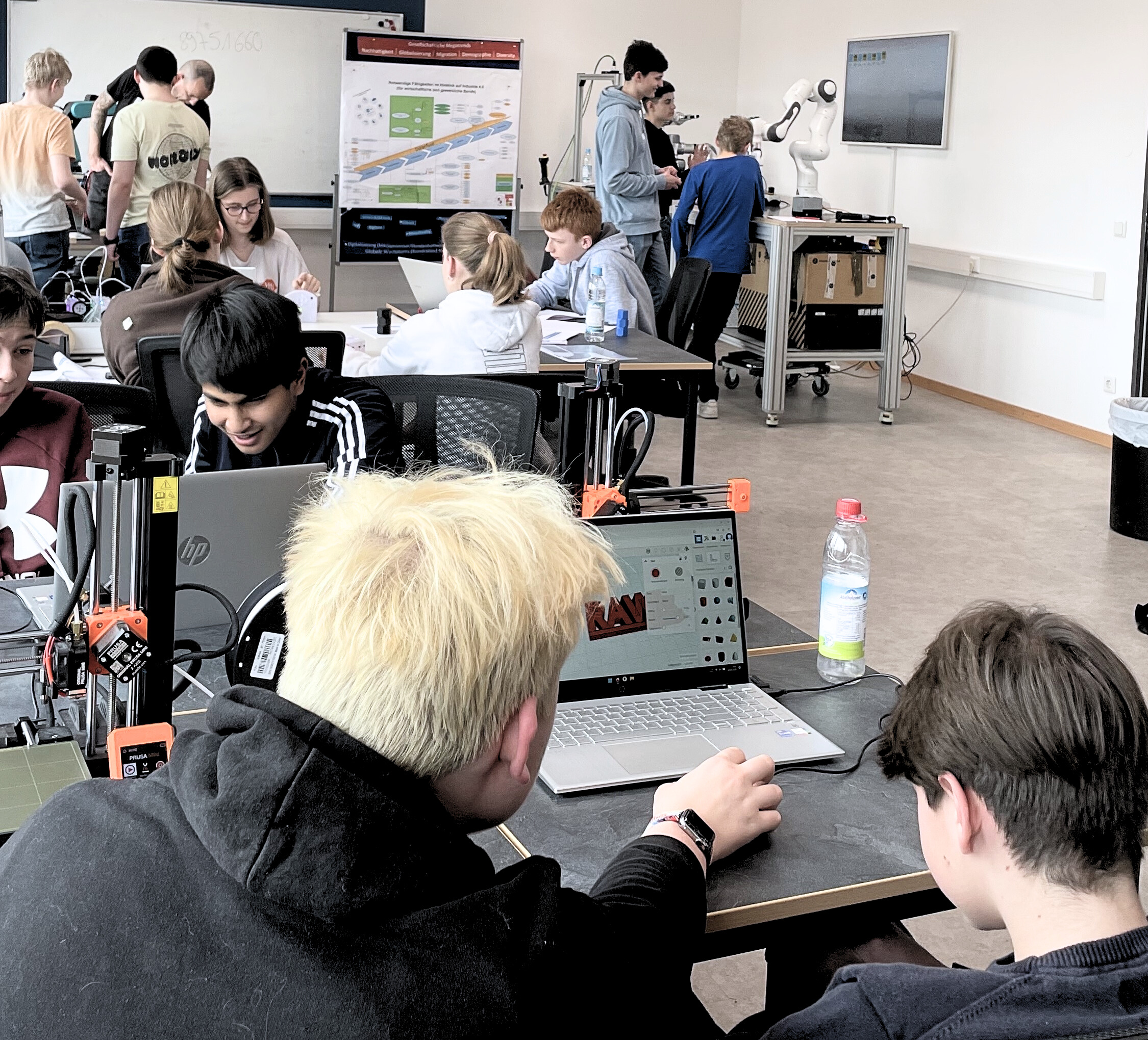 Auszubildende arbeiten in einem modernen Schulungsraum mit 3D-Druckern und kollaborativen Robotern an Projekten zur digitalen Fertigung.