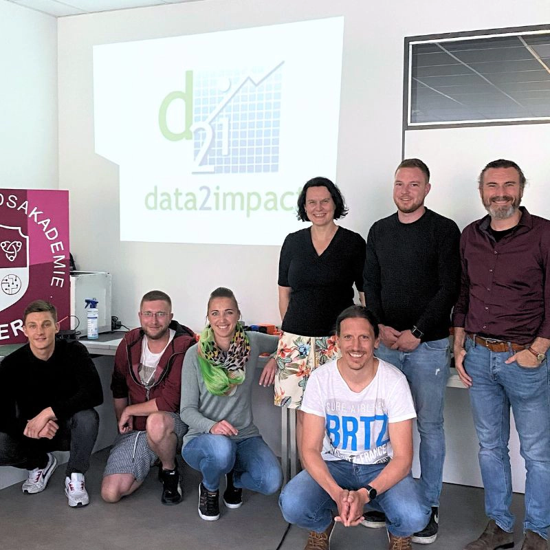 Gruppenfoto eines erfolgreichen Coding-Kurses bei GAMunich mit Projektorfolie „data2impact“ im Hintergrund.