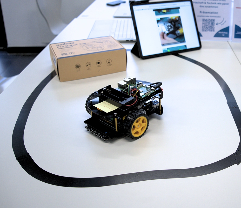 Kleiner Roboter mit gelben Rädern folgt einer schwarzen Linie auf einem Tisch – Coding-Projekt mit Tablet und Kit.