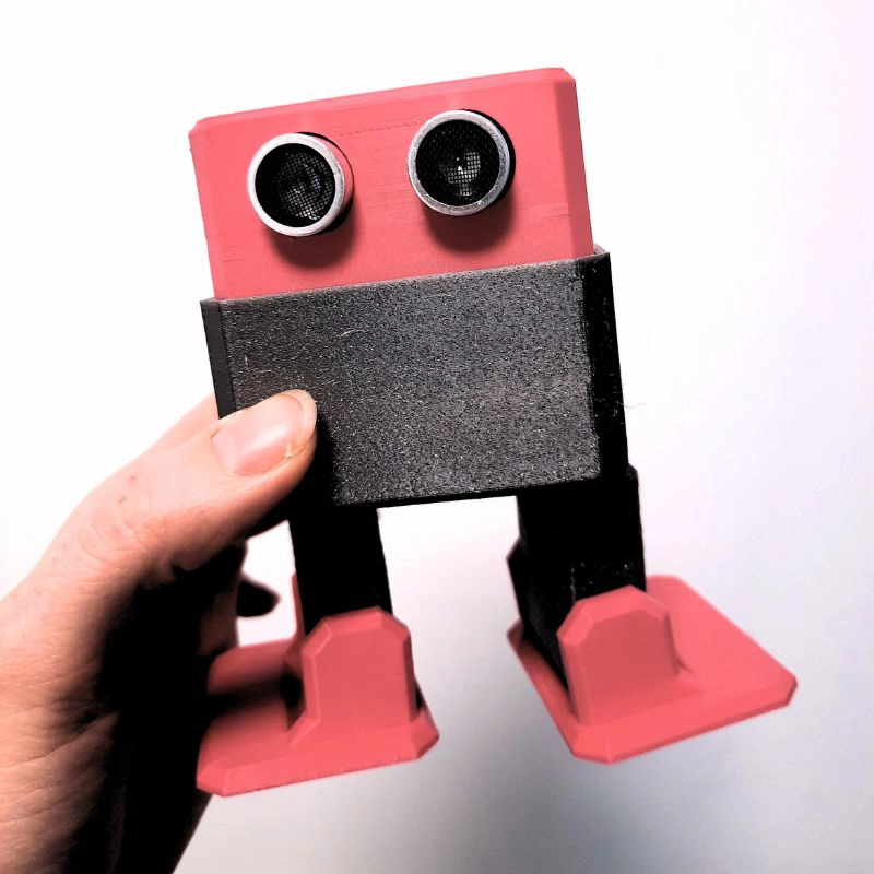 Hand hält kleinen DIY-Roboter mit Ultraschallsensoren als Augen – spielerisches Coding-Projekt für Einsteiger.