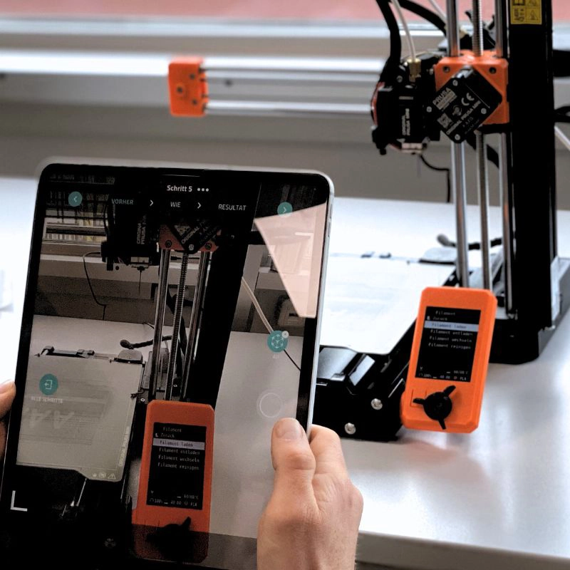 Tablet zeigt AR-gestützte Schritt-für-Schritt-Anleitung zur Bedienung eines 3D-Druckers im Rahmen eines Industrie 4.0 Trainings.