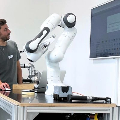 Teilnehmer beobachtet kollaborativen Roboterarm bei einer Industrie 4.0 Schulung mit Bildschirmsteuerung.