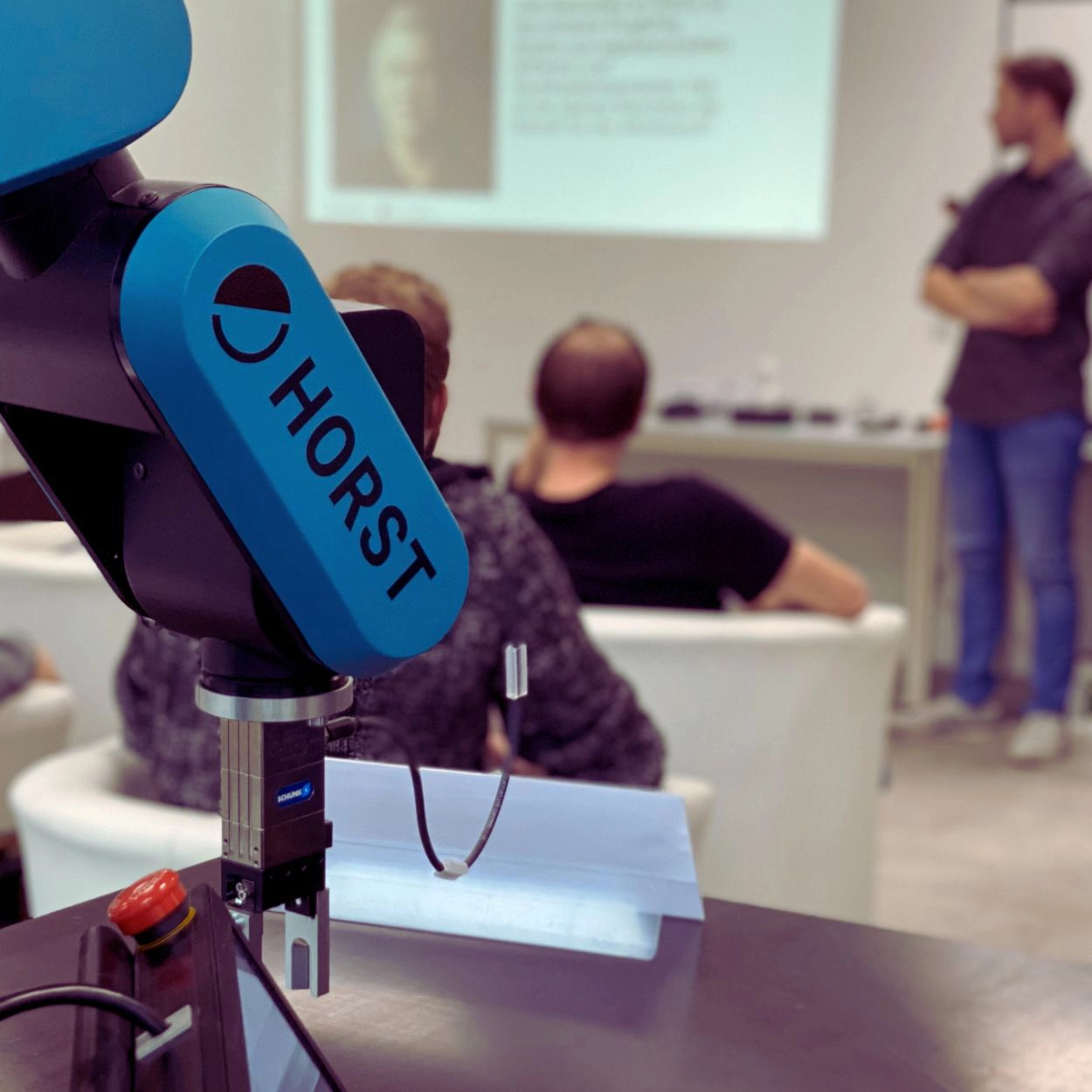 Industrieroboter HORST in einem Mitarbeiterschulungskurs mit Vortrag im Hintergrund zu neuen Automatisierungstechnologien.