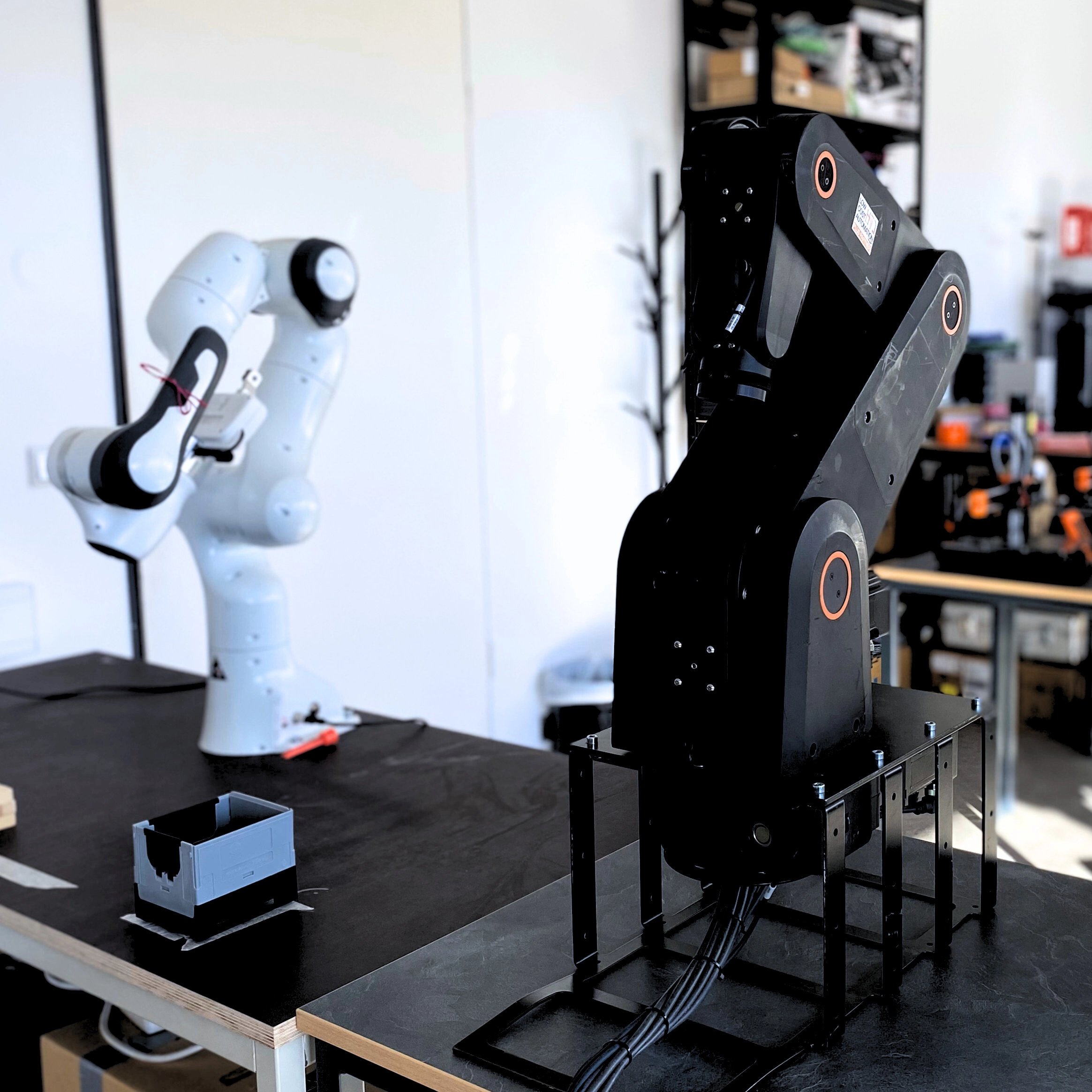 Zwei moderne Roboterarme stehen auf Arbeitstischen in einem Technikraum zur Schulung im Bereich Robotik.