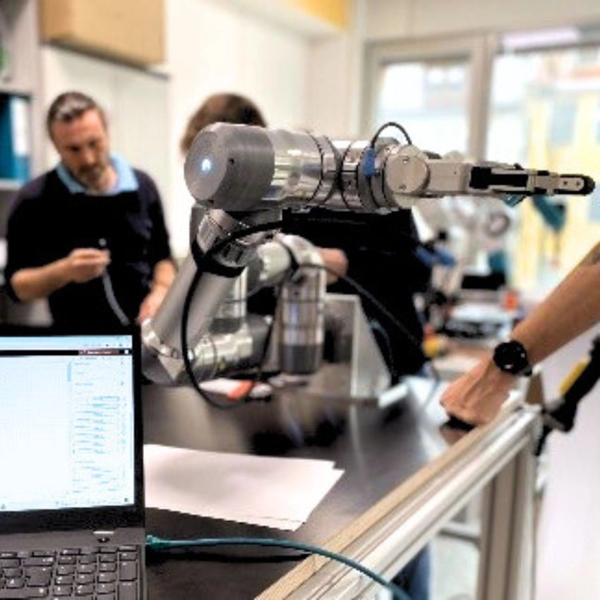 Teilnehmer arbeiten mit kollaborativem Roboterarm an einem Robotik-Trainingsprojekt und programmieren über Laptop.