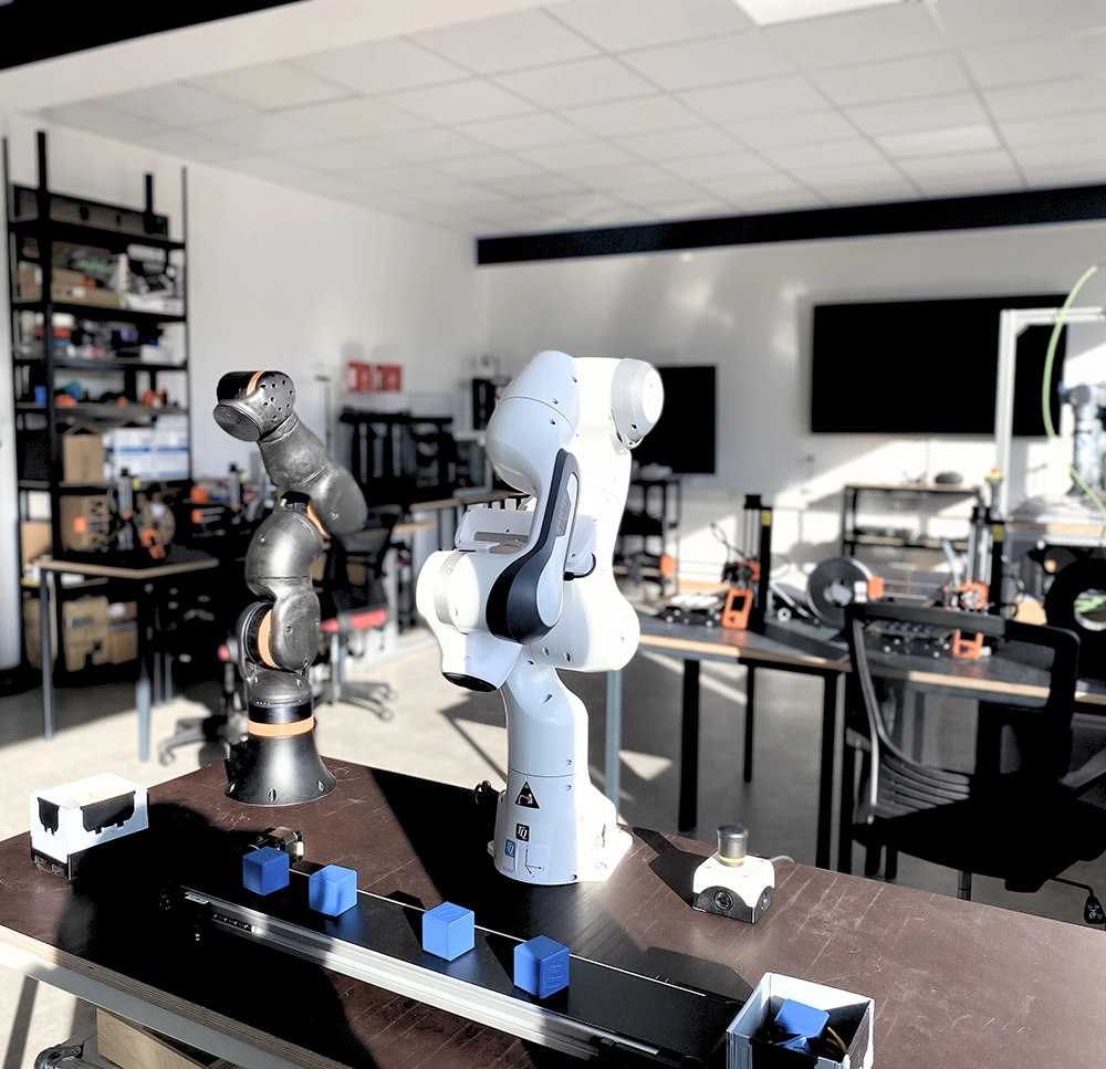 Zwei kollaborative Roboterarme in einem modernen Technikum, umgeben von 3D-Druckern und technischen Lernstationen.